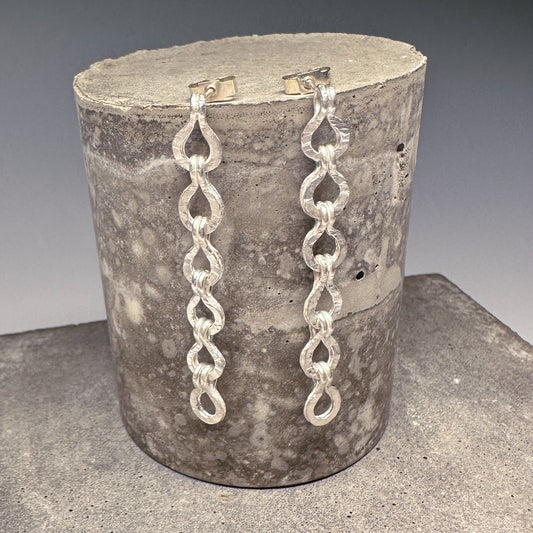 Silver roman chain drop earrings on concrete block